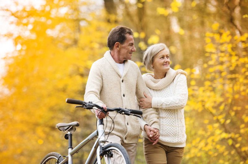 Elderly couple walking through a fall forest with a bicycle.